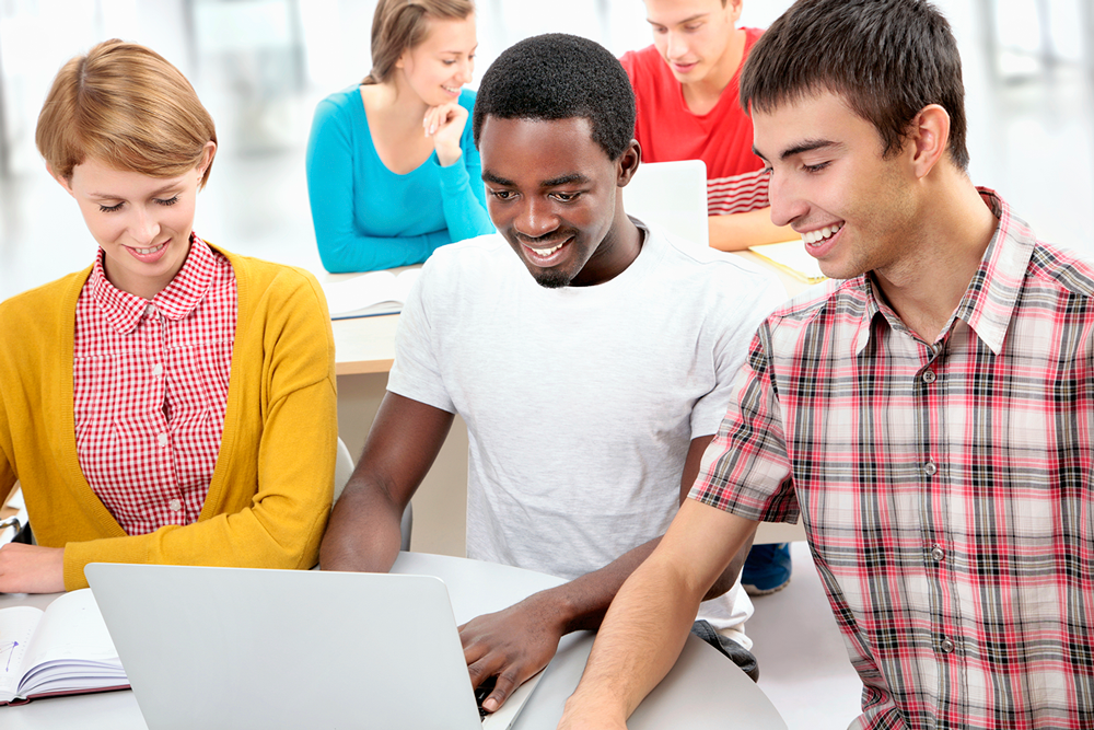 Three young financial services students sit around a table looking at a laptop. They are casually dressed and smiling.