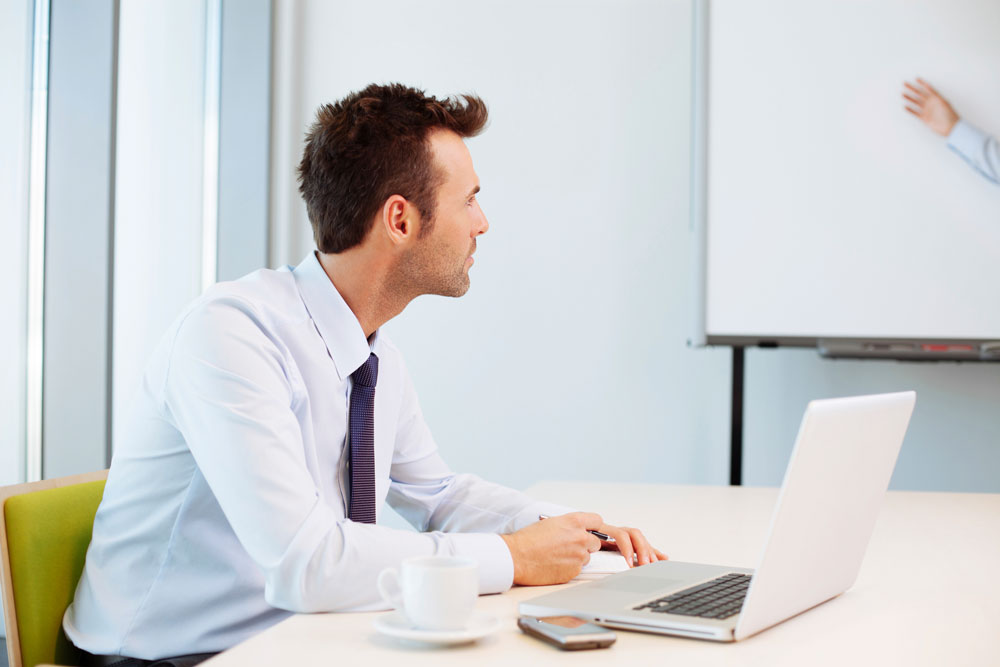 A male financial services student in business attire watches his tutor delivering a financial service training course.