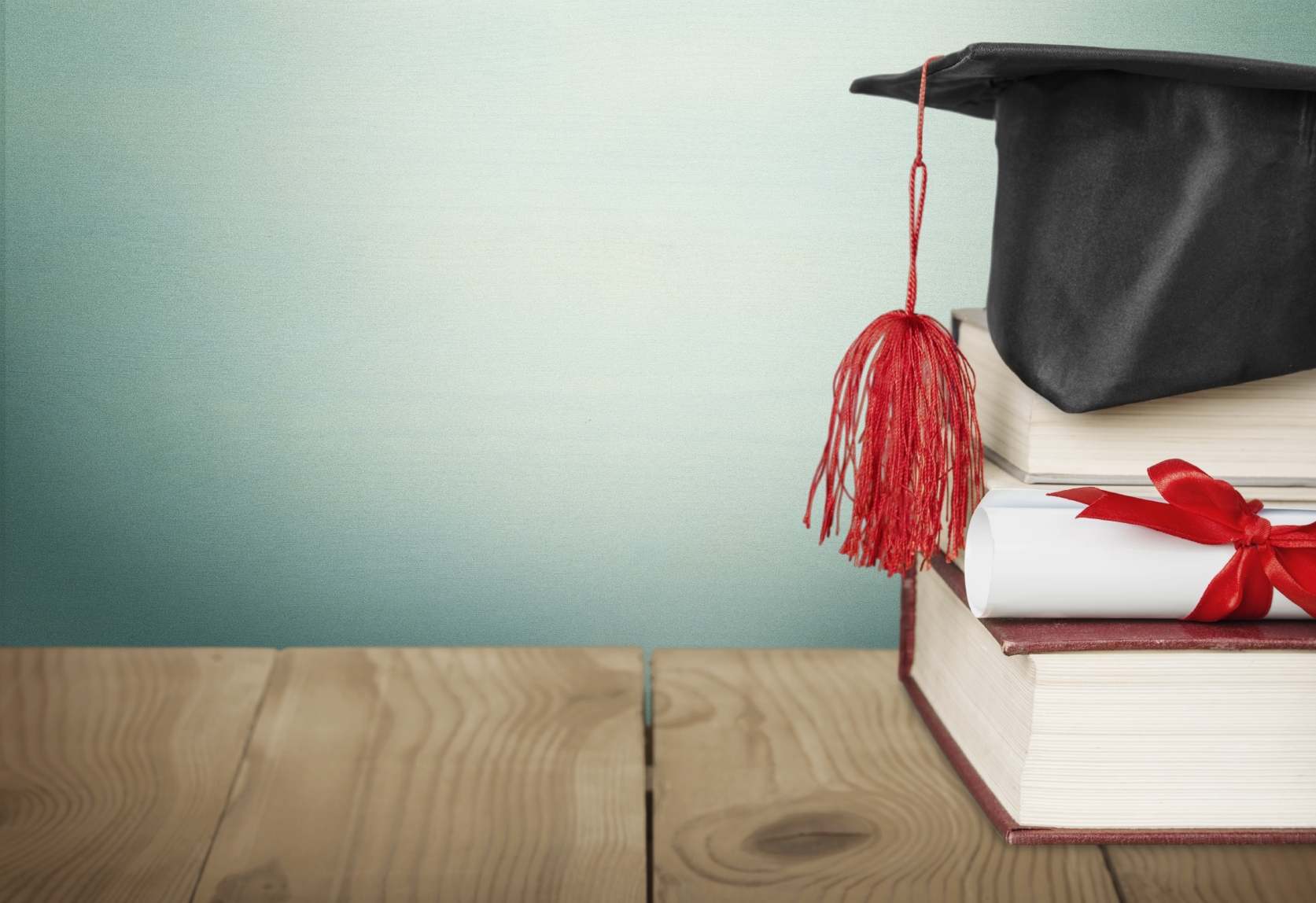 Financial Services study concept image. A black graduate cap sits on top of a pile of books against a green background.