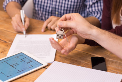A man signs a mortgage contract while the mortgage adviser or estate agent hands over house keys to a woman.