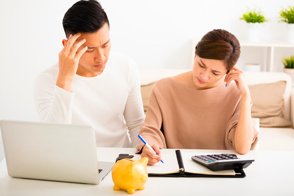 A young Asian man and woman look worried as they use a calculator to complete financial advice or budgeting paperwork.