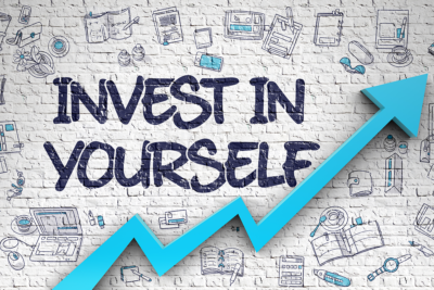 Training concept. The words 'Invest in Yourself' appear in blue against a white wall, an arrow underneath points upwards.
