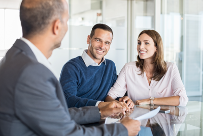 A male mortgage adviser offers financial advice to a man and a woman. The couple are both smiling at the financial adviser.
