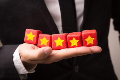 A man wearing a black suit holds a row of five red wooden blocks on the palm of his hand. Each block has a gold star on it.