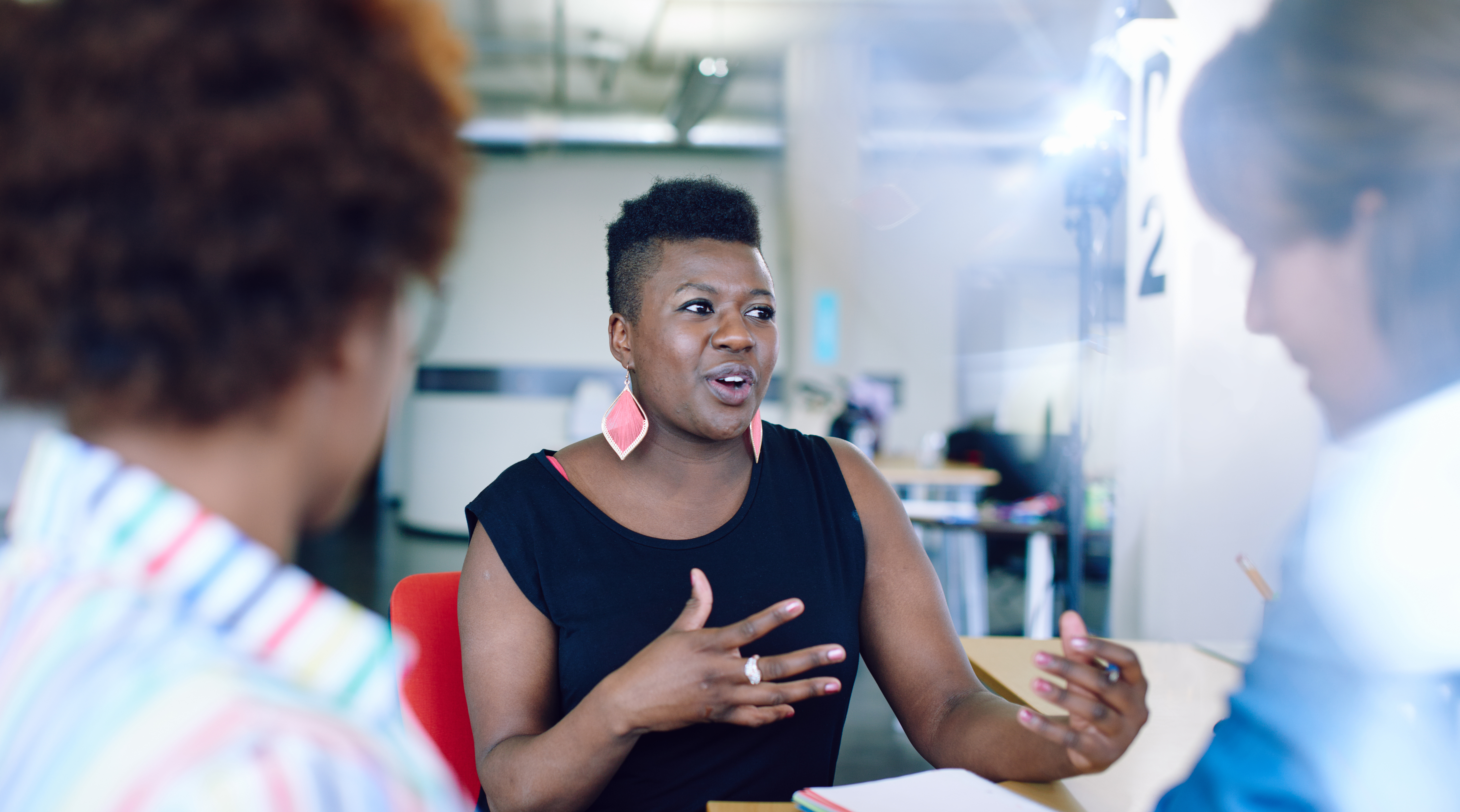 A Black female mortgage advisor lecturer in casual attire talks to a group of financial services students. She has a friendly smile on her face.