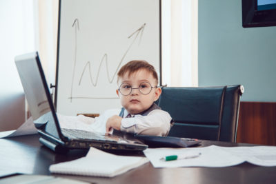 Financial Services Training concept. A young child in business wear sits at a desk covered with financial reports.