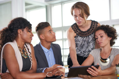 A group of young business people gather round a screen at a table