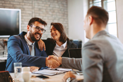 Three business people laughing and shaking hands at a table