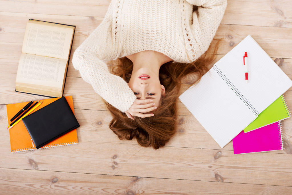 Girl lying on floor surrounding by exam books