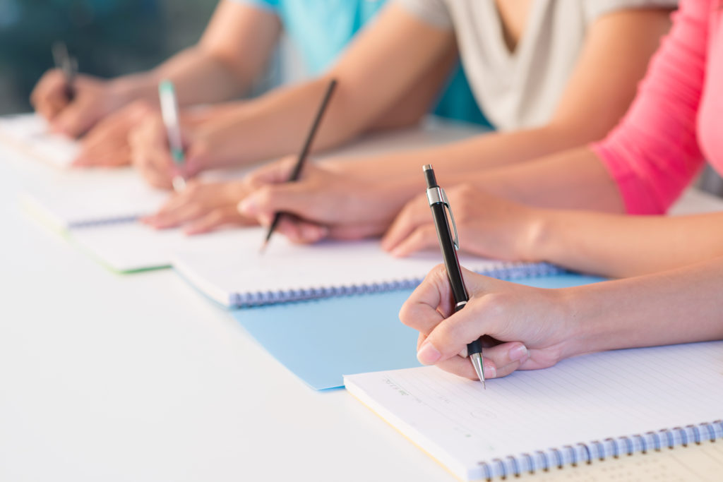 Close up of four pairs of women's hands writing on notepads in a financial services training course.