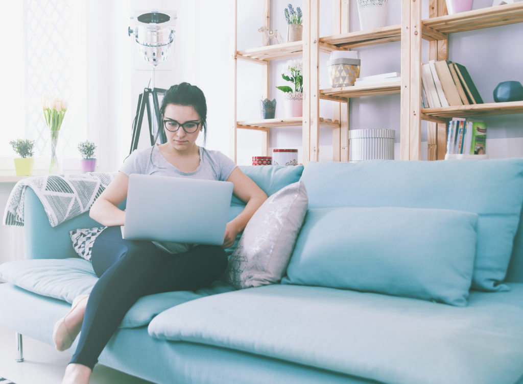 Woman working from home sat on a sofa with a laptop on her knee