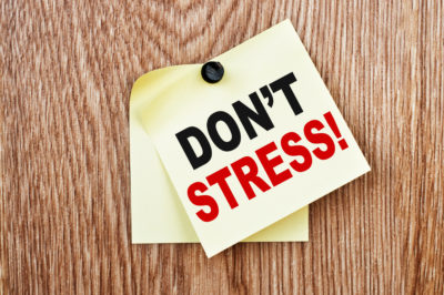 Don't Stress concept image. The words 'Don't Stress' are printed on a yellow sticky note against a wooden background.