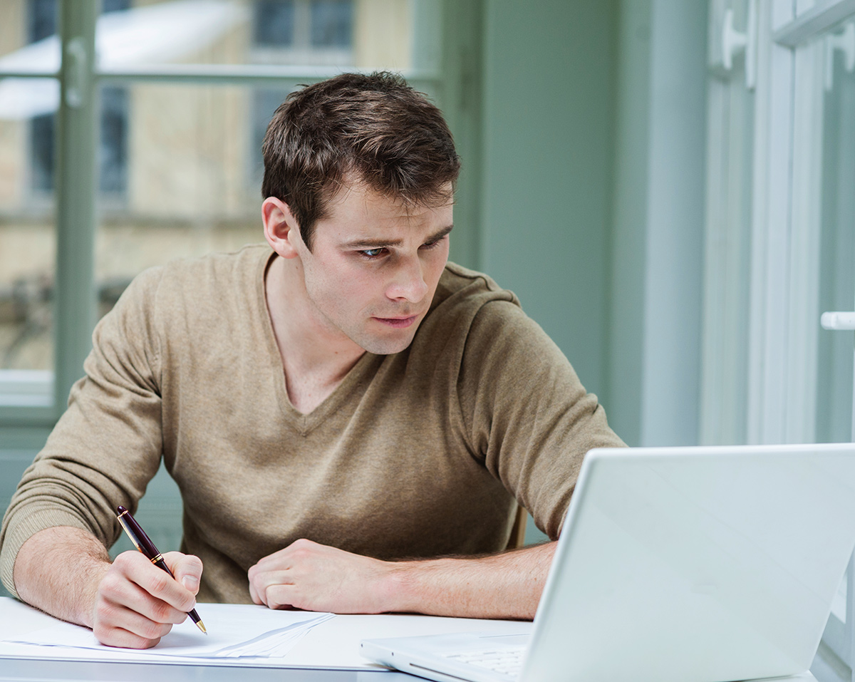 Man takes notes whilst looking at a laptop