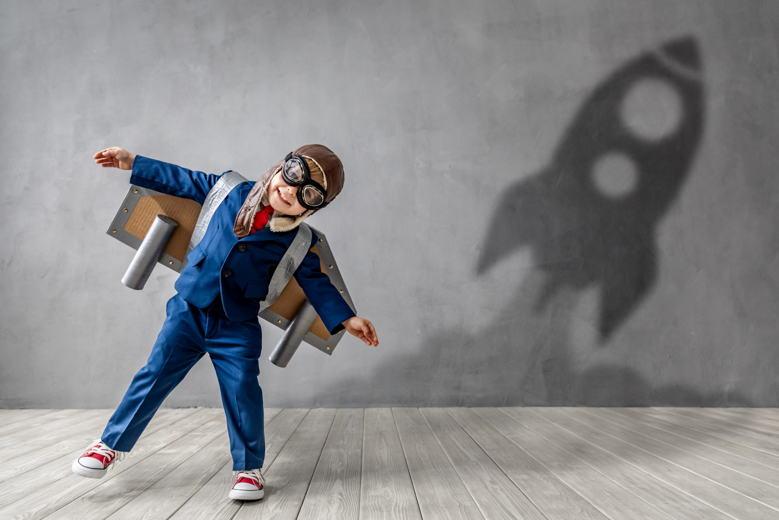 Young boy in a blue suit and cardboard wings creating a tilted rocket ship shaped shadow