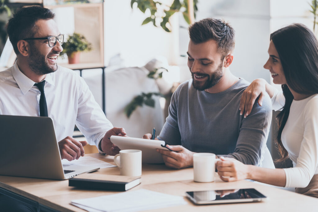 Mortgage advisor chatting to young couple signing a contract at a desk.