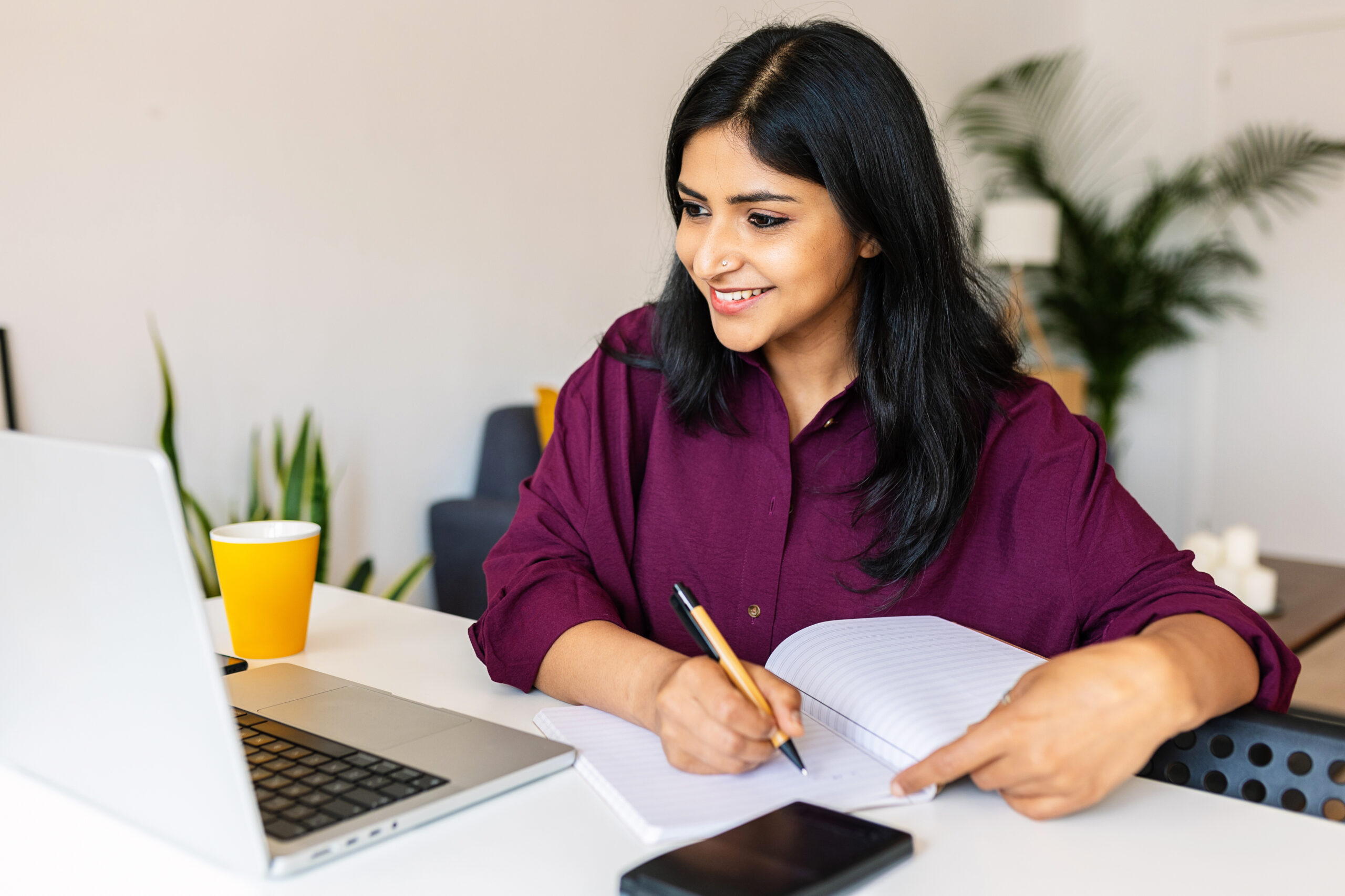 A young woman makes notes on paper while working on an online course.