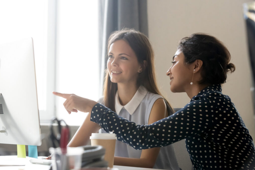 Two young women looking at a computer screen with one of them pointing to it.
