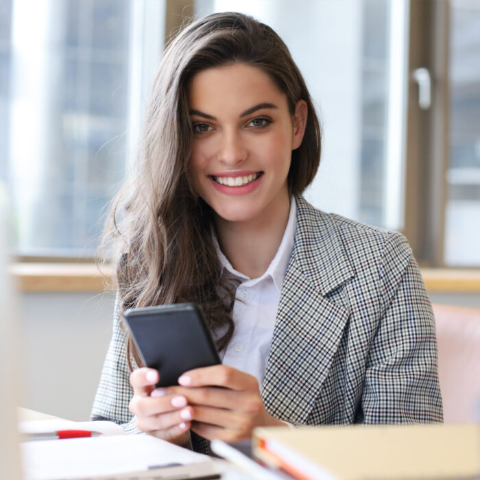 A young woman with a mobile phone in her hands smiling.